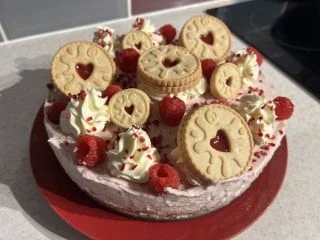 Delicious homemade cake decorated with whipped cream, raspberries, and jam-filled heart-shaped biscuits.