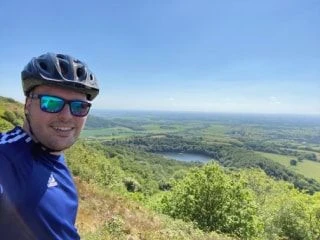 Person cycling on a rural road surrounded by nature, wearing a helmet and athletic gear, capturing an active outdoor lifestyle.