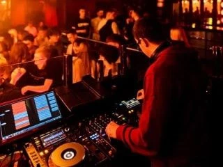 DJ using a professional mixing console with vibrant lighting effects, showcasing live electronic music performance equipment.