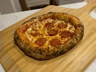 Freshly baked pepperoni pizza with a bubbly, golden crust served on a wooden pizza peel.
